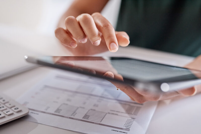 Nahaufnahme einer nicht erkennbaren Geschäftsfrau, die ein digitales Tablet benutzt, während sie in einem Büro Papierkram durchgeht
