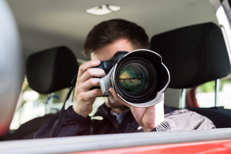 Seitenansicht eines Privatdetektivs, der im Auto sitzt und mit einer Slr-Kamera fotografiert